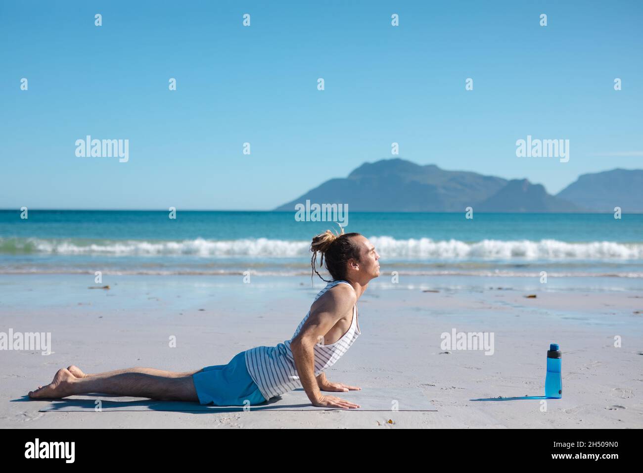 Man practicing cobra pose yoga on mat at beach against blue sky with copy space Stock Photo