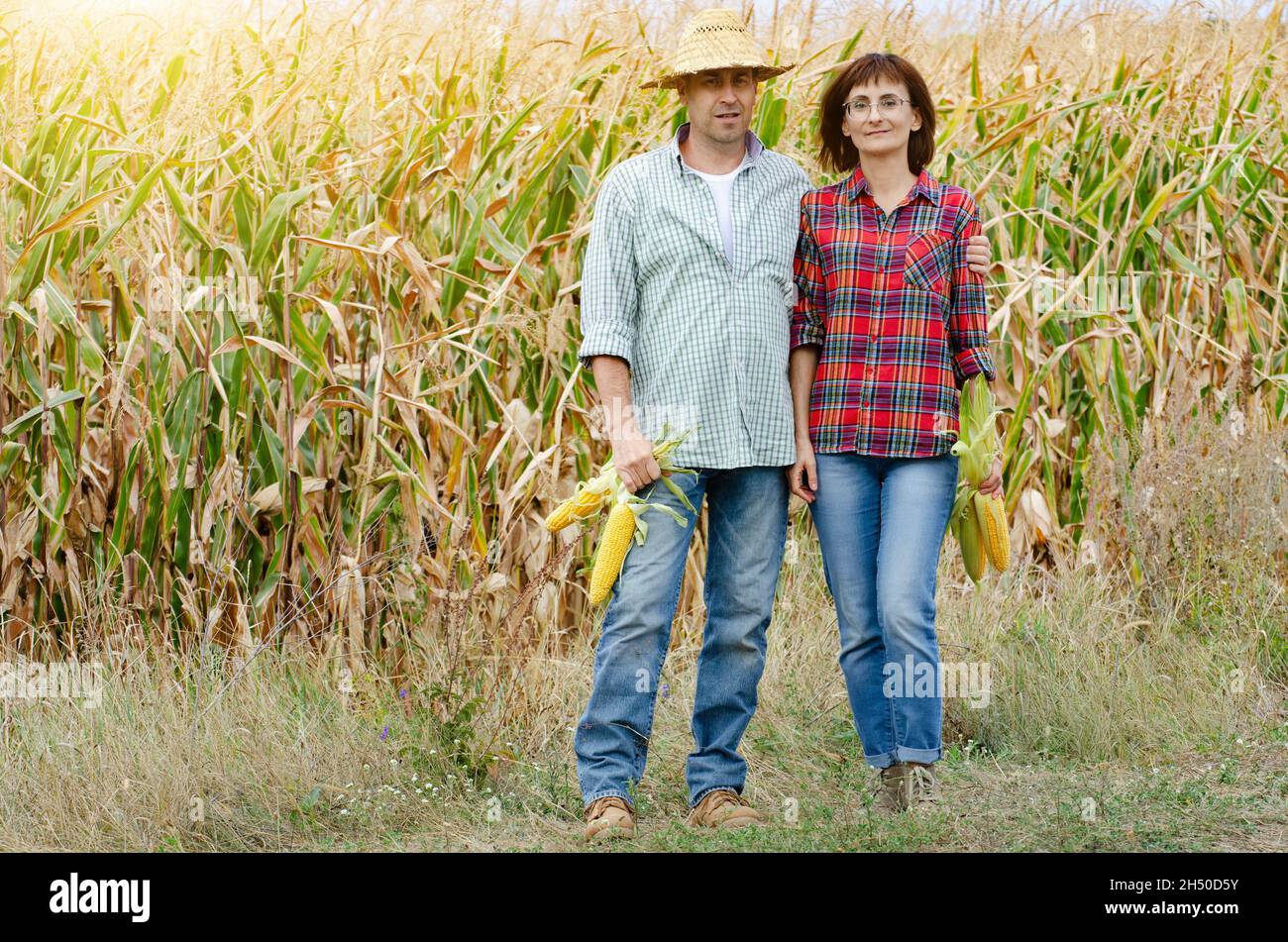 Caucasian middle age farmer family of two stands by maize field with