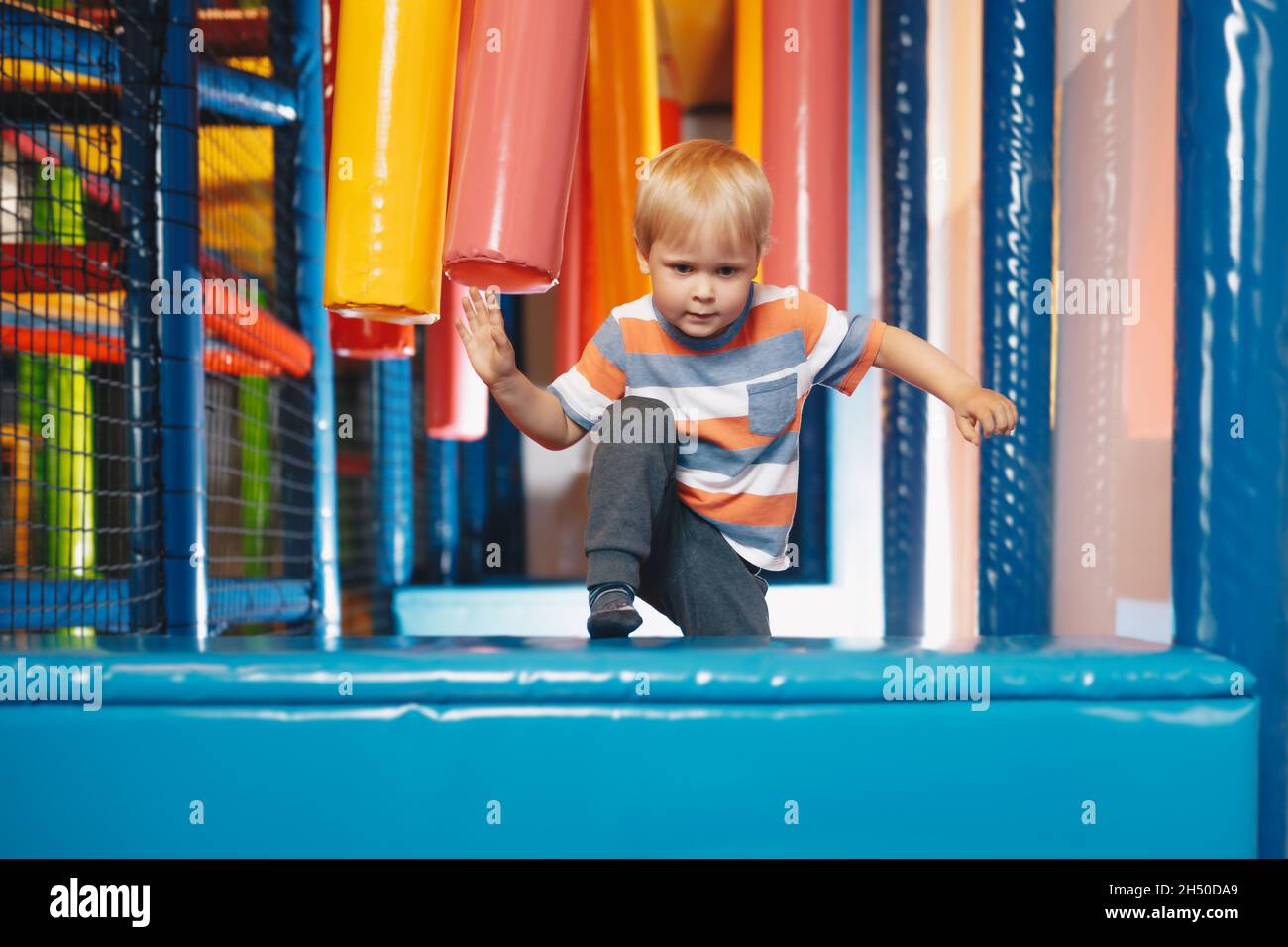 Happy boy jumping over obstacles in a Indoor playground. Kid jumping on playground cushions. Child having fun on modern playground. Cute kid playing o Stock Photo