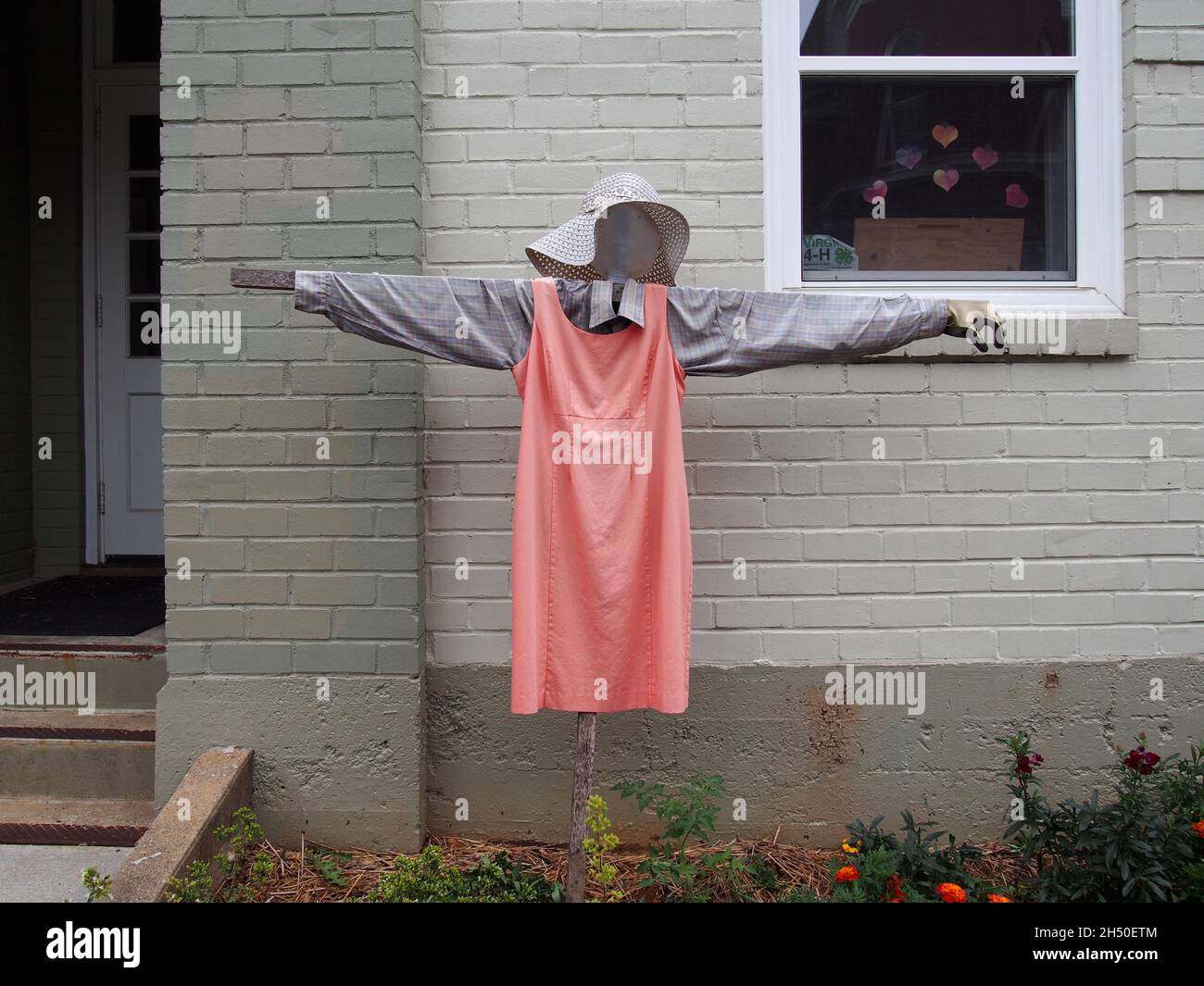 A scarecrow decoration in front of a painted brick wall, window and entrance, USA, 2021 © Katharine Andriotis Stock Photo