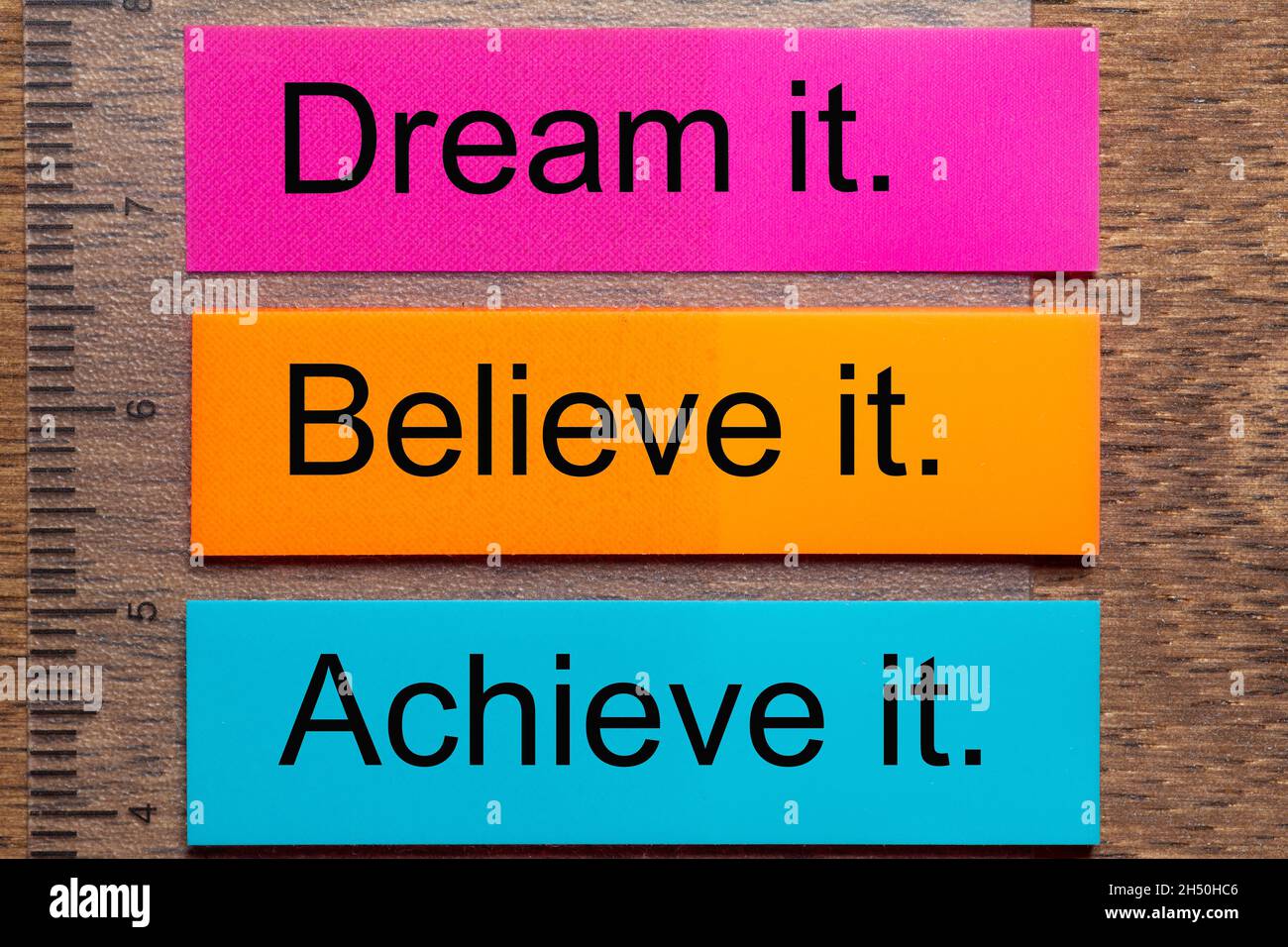 Three bookmark stickers with the words dream it, believe it, achieve it, on a dark natural wooden table Stock Photo