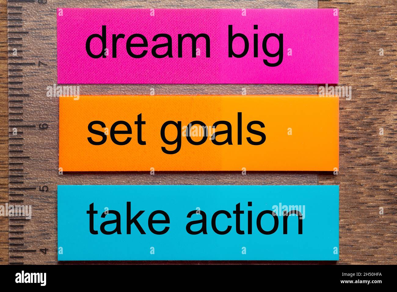 Three bookmark stickers with the words dream big, set goals, take action on a dark natural wooden table Stock Photo