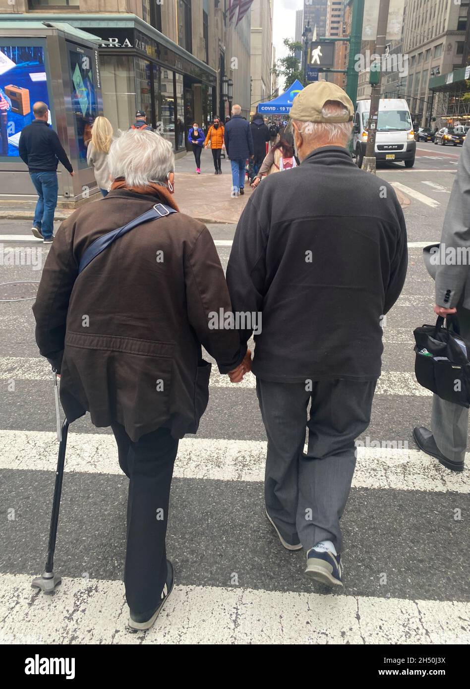 Senior couple walk hand in hand crossing 42nd Street  along 5th Avenue in midtown Manhattan in the autumn. Stock Photo
