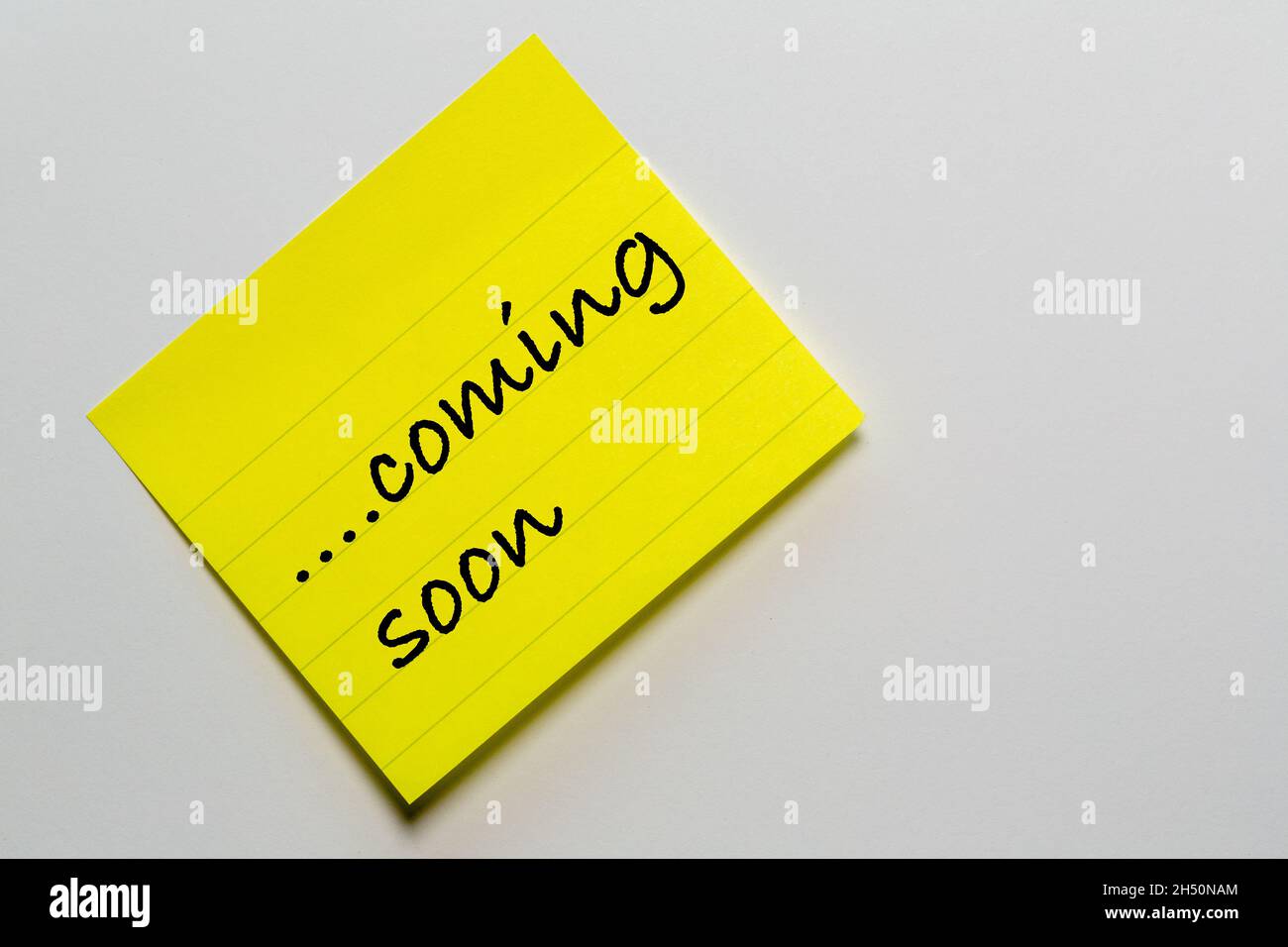 yellow note sticker diagonally against a white background stylized handwriting with the text: coming soon Stock Photo