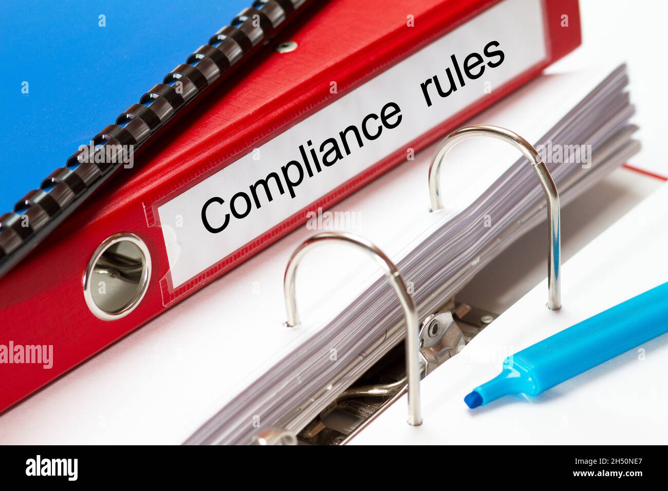 large red folder for compliance rules including blue ring binder and blue maker Stock Photo