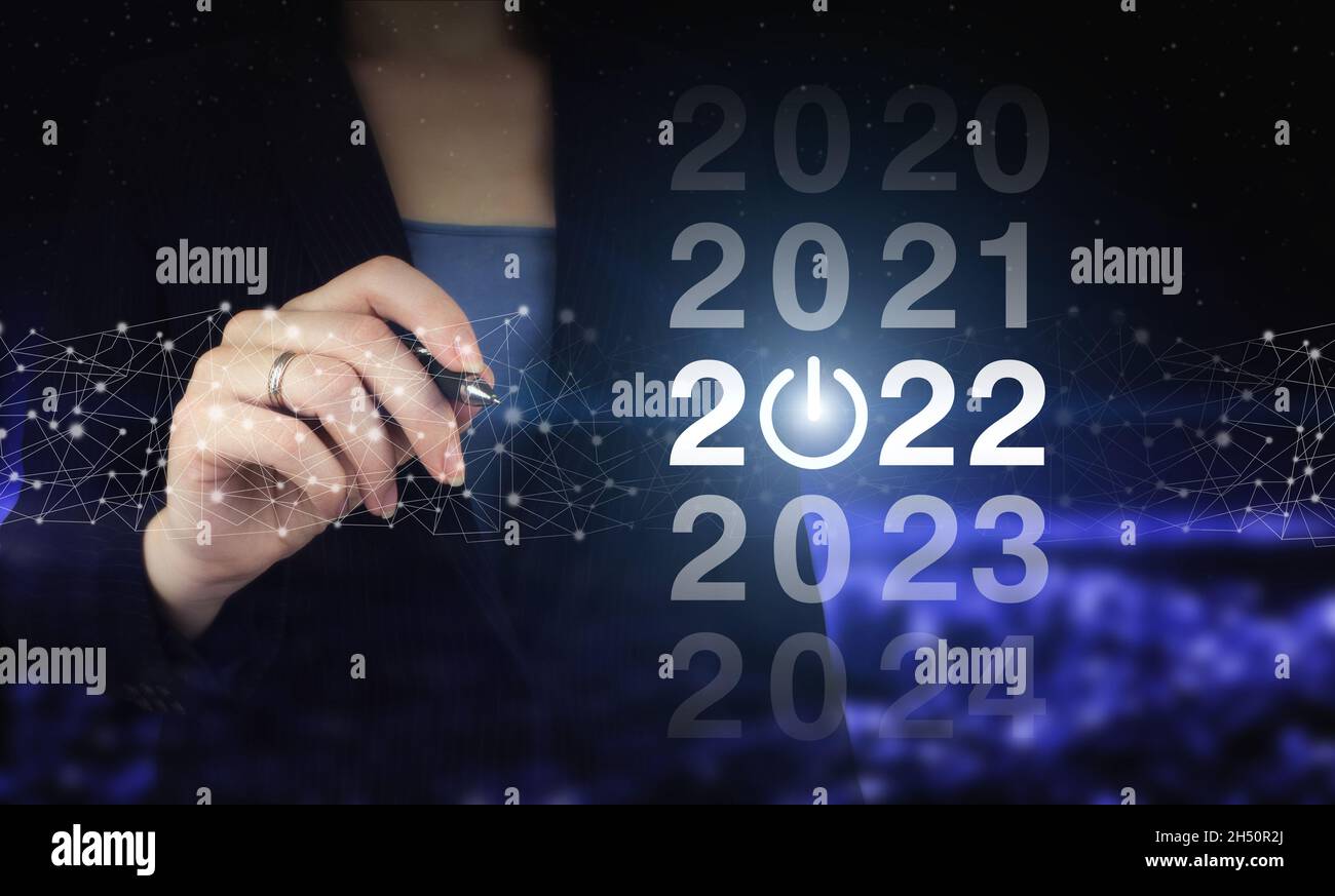 2022 new year. Hand holding digital graphic pen and drawing digital hologram 2022 sign on city dark blurred background. Concept Start New Year 2022 Stock Photo