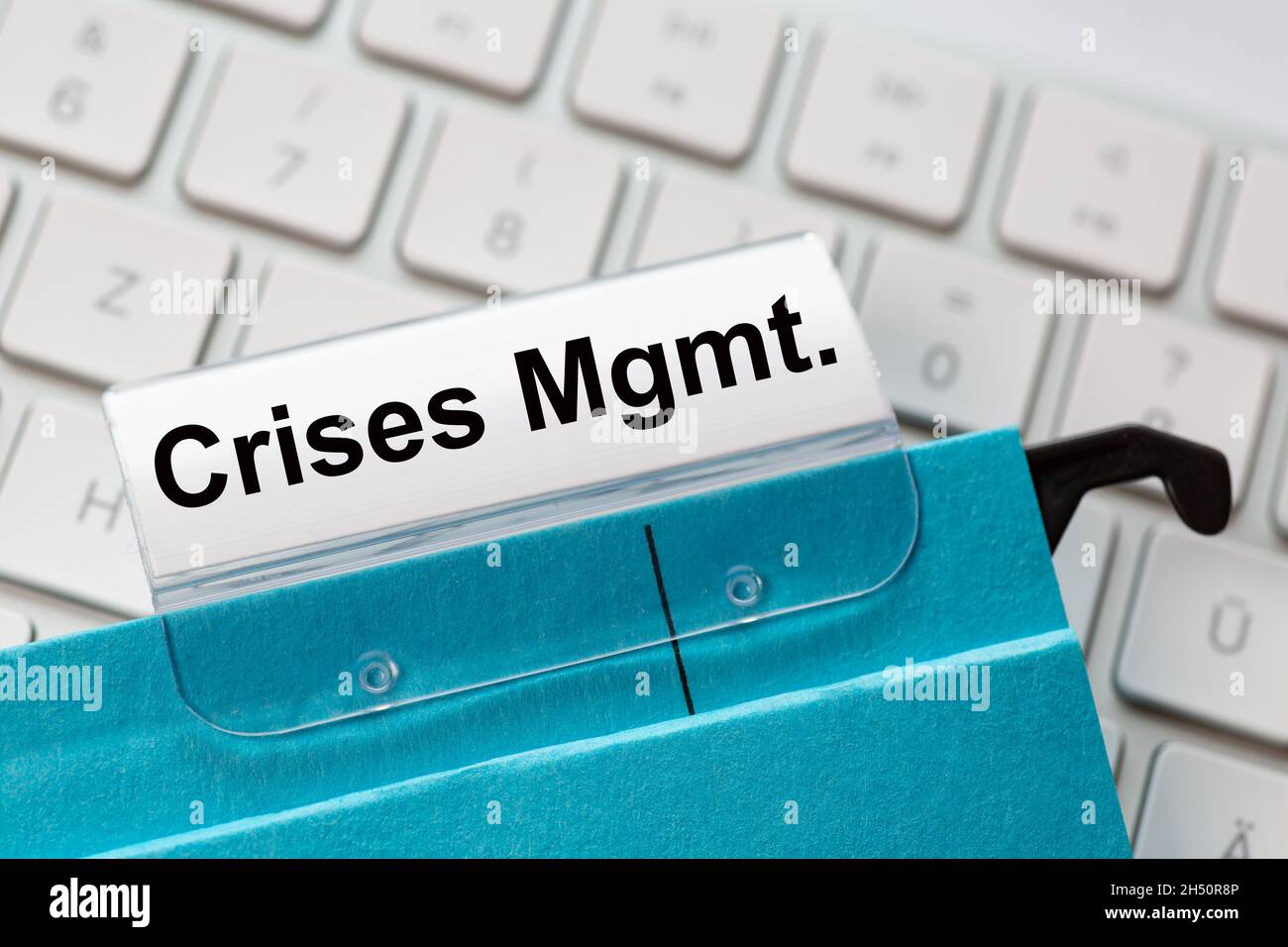 The words  crises Management can be seen on the label of a blue hanging folder. The hanging folder is on a computer keyboard. Stock Photo