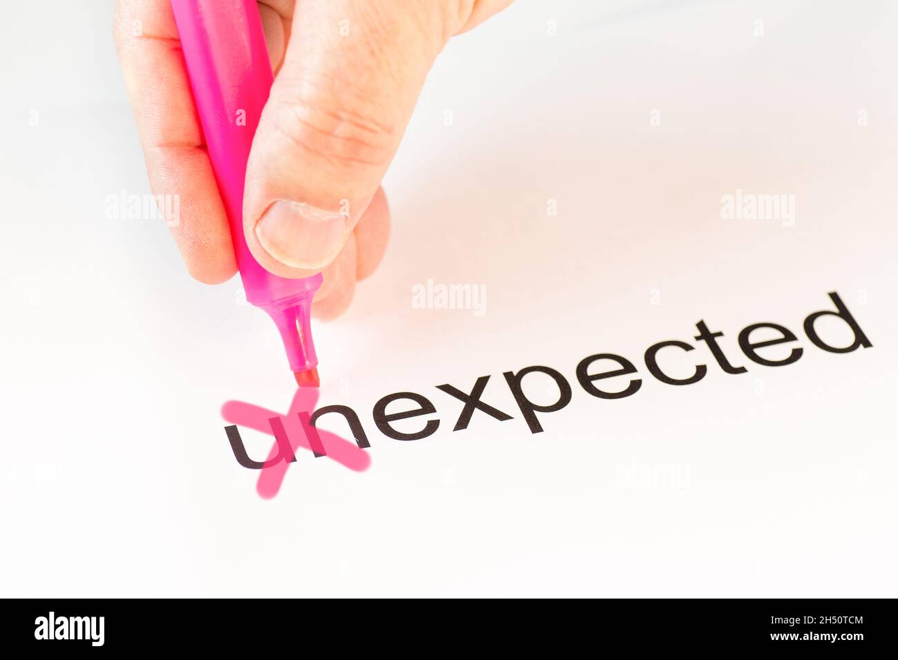 The prefix 'un' of the word unexpected is crossed out with a pink pencil by a hand Stock Photo
