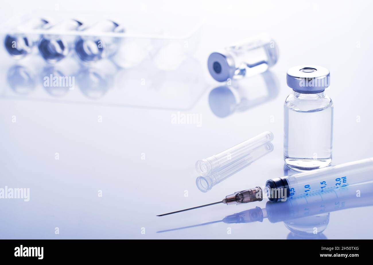 Single use syringe for injection treatment on medical table with vials of liquid drug doses flu shots at background. Vaccination or immunization care Stock Photo