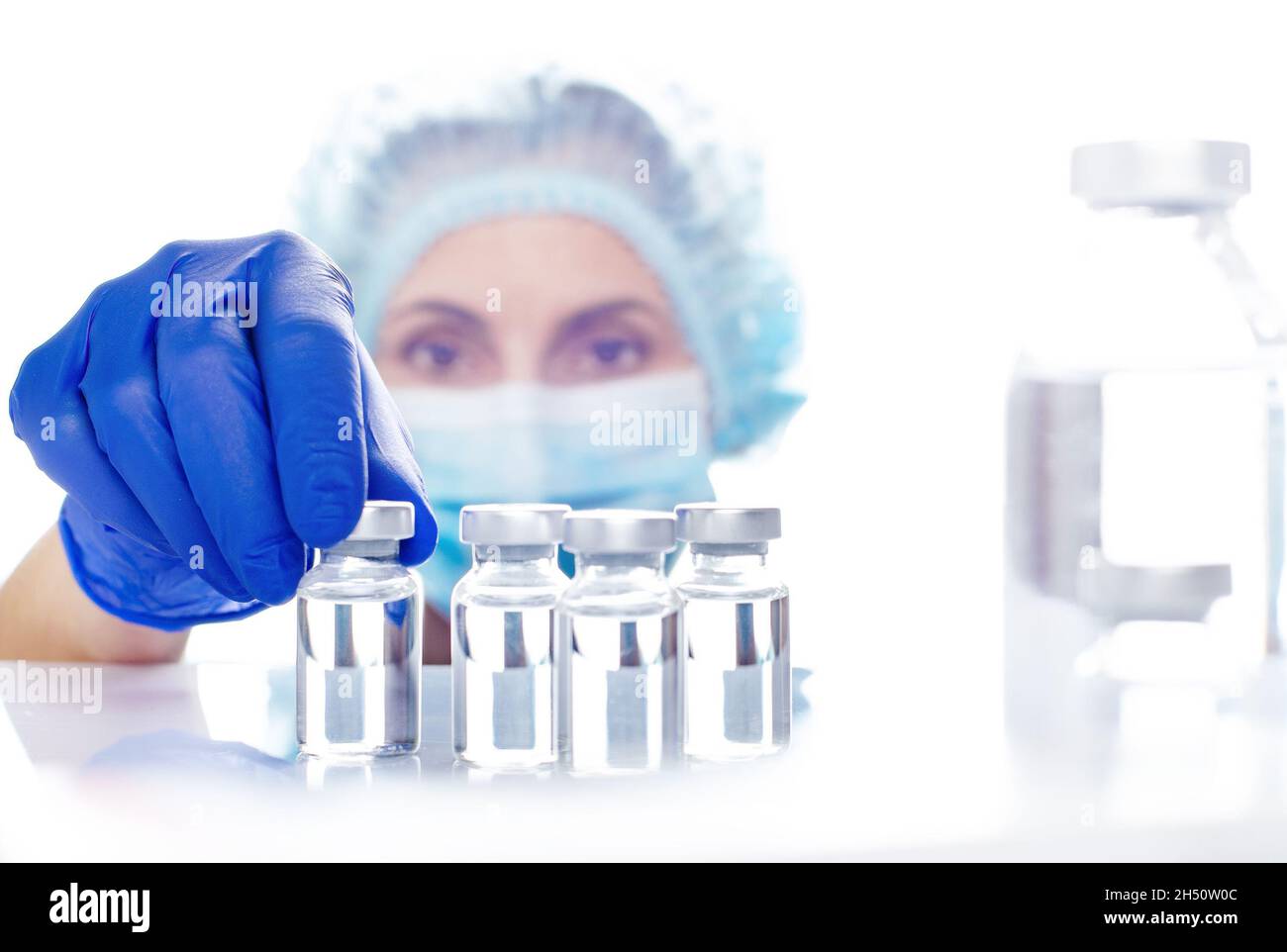 Female nurse in safety mask and gloves takes vial with liquid medicine from refrigerator shelf Stock Photo