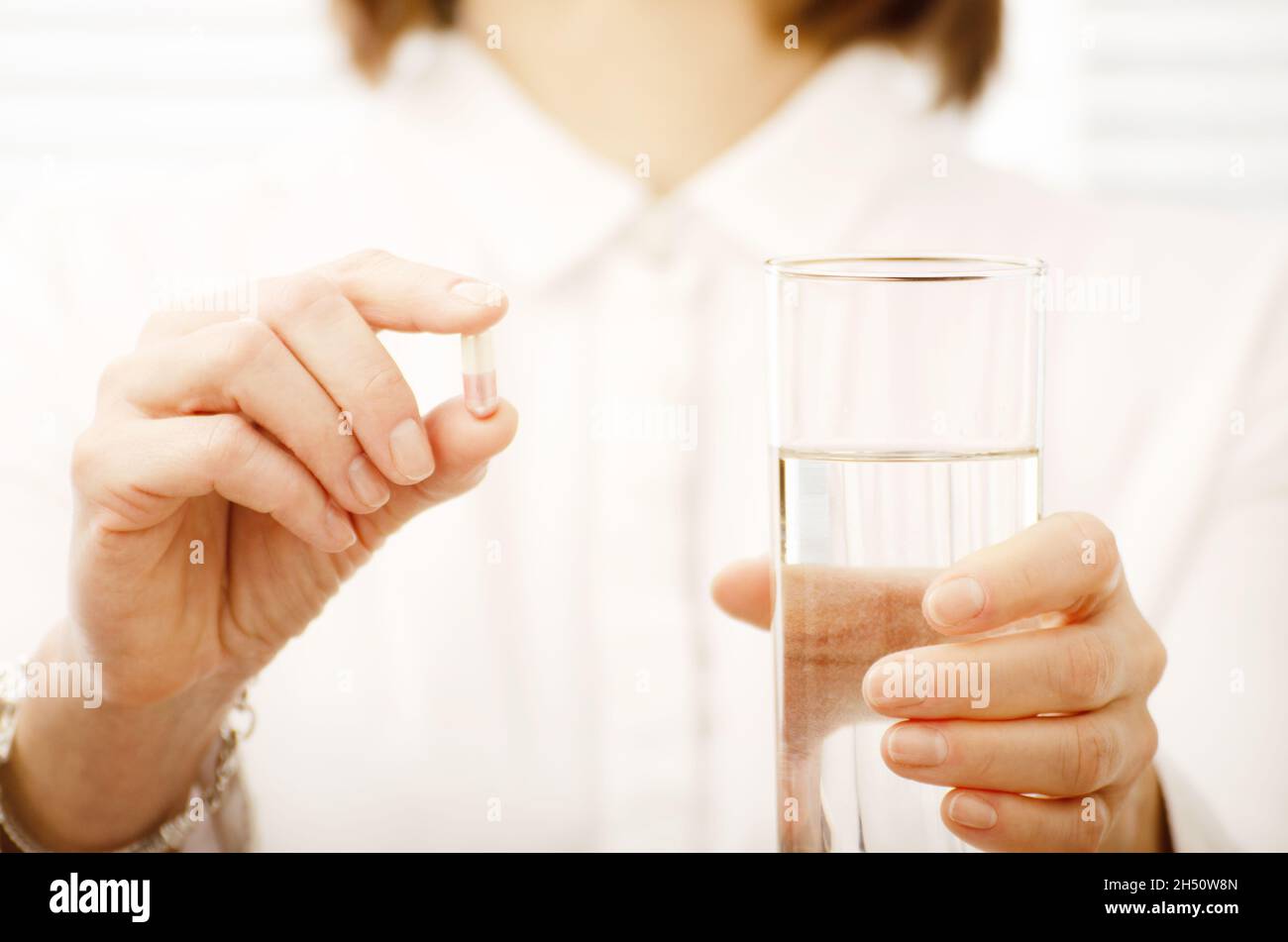 Caucasian female model holds pill and glass of water in her hands closeup Stock Photo