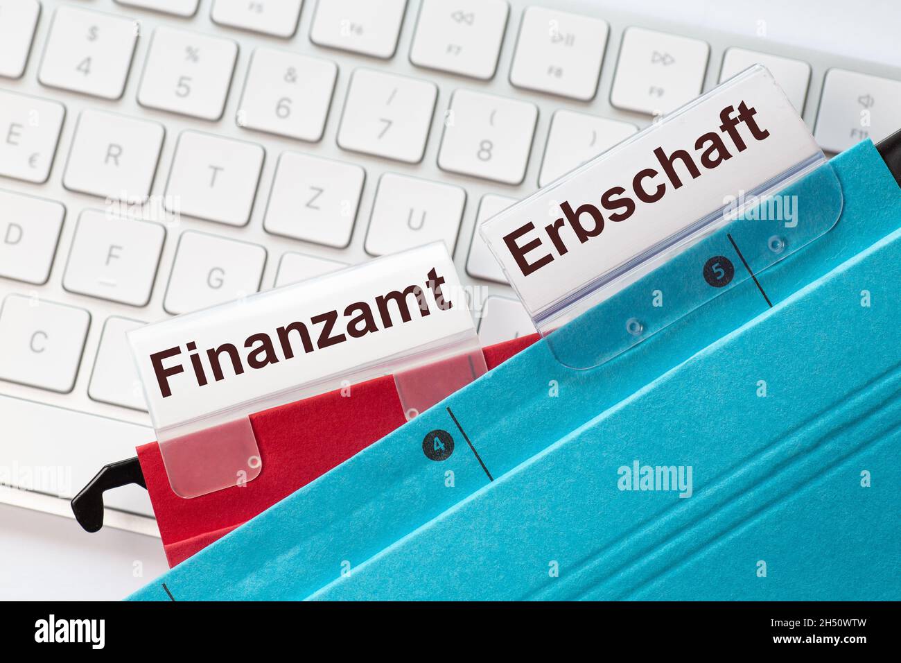 The German words tax office and inheritance can be seen on the labels of a red and blue hanging folders. The hanging folders are on a computer keyboar Stock Photo