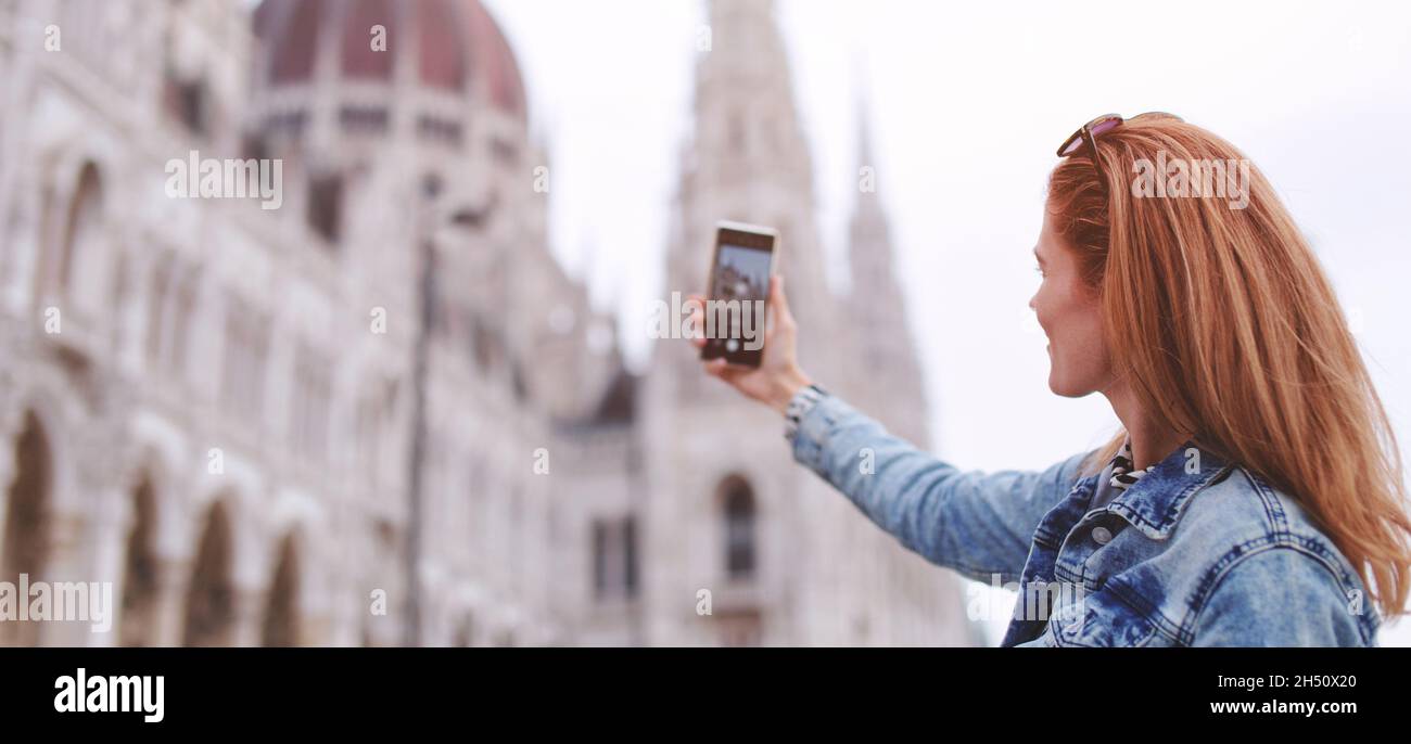 Young redhead woman taking photo of Hungarian Parliament building at Budapest, Hungary banner Stock Photo