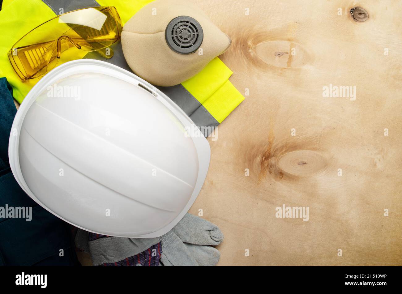Flat lay view at yellow plastic hard hat, glasses, respirator, reflective vest and protective gloves laying on plywood. Safe labor concept Stock Photo