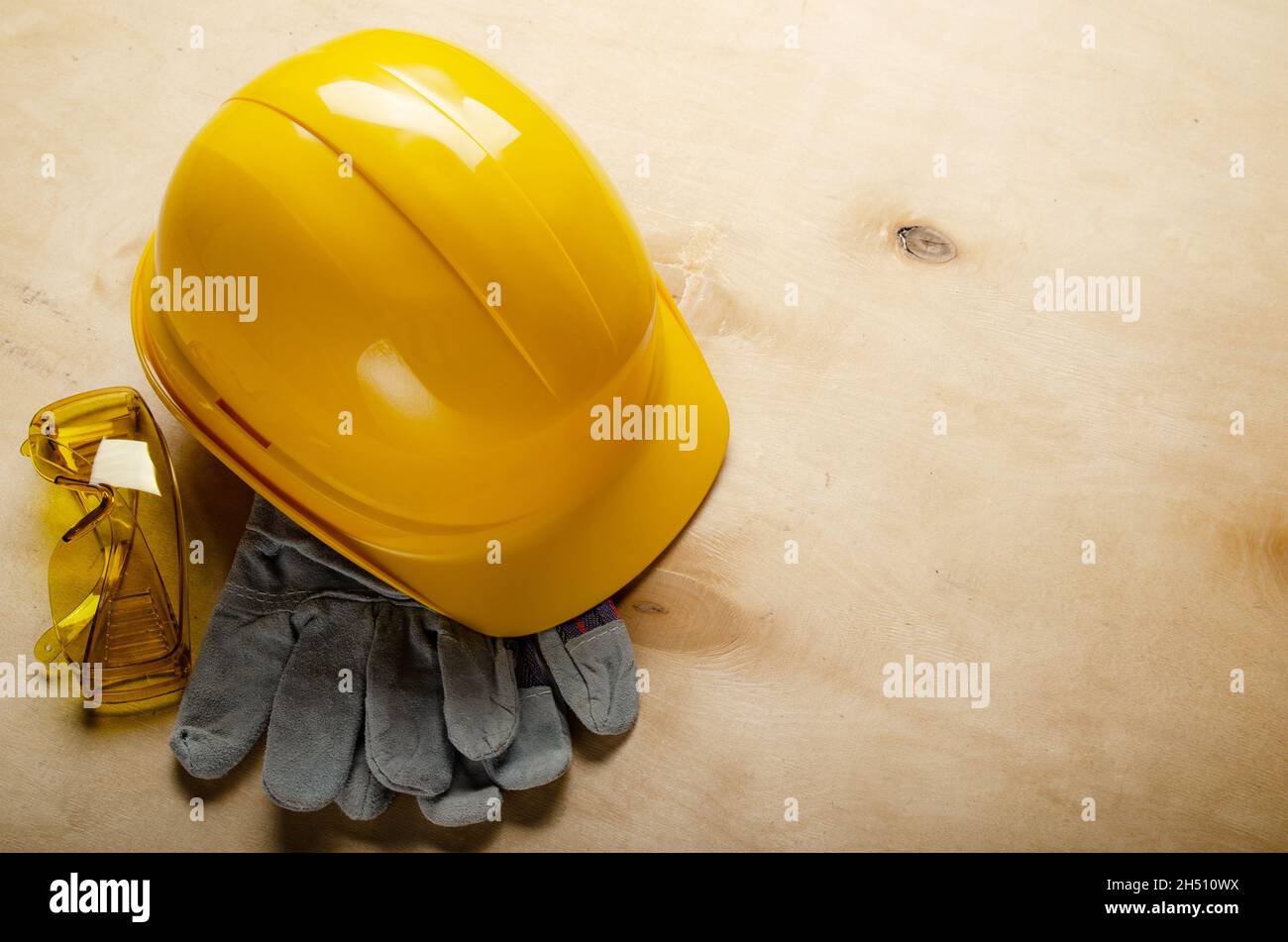 Yellow plastic hard hat glasses and protective gloves laying on plywood. Safe labor concept Stock Photo