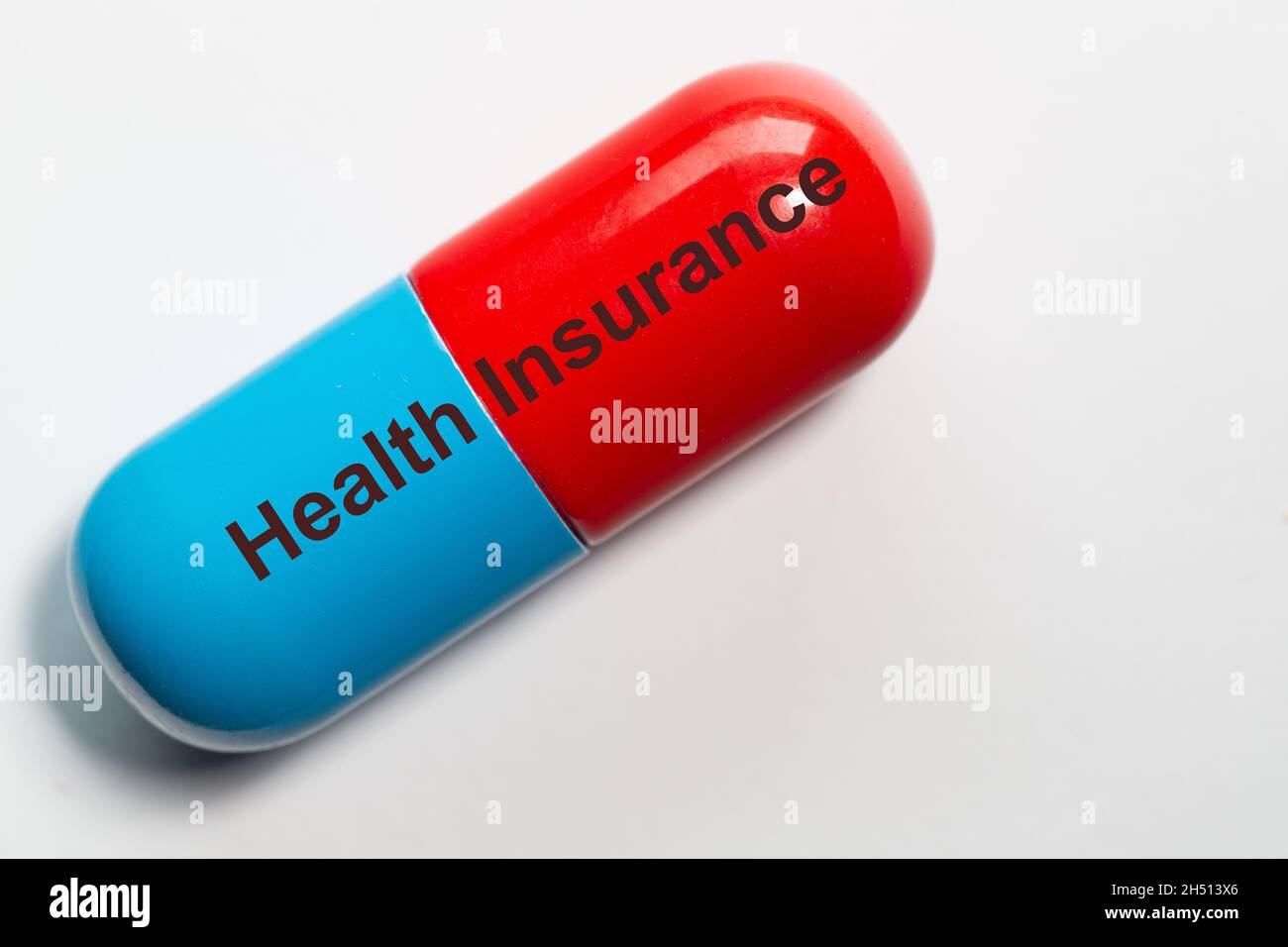 a pill in blue and red as a smbol photo has the words  Health Insurance on it. The pill is isolated against a white background. Stock Photo