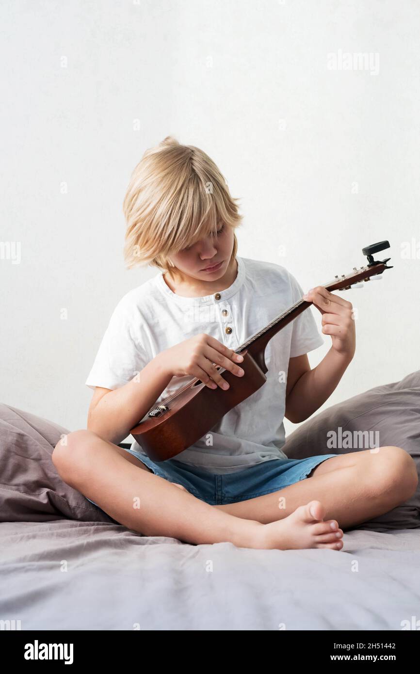 A boy wearing a face mask plays ukulele in front of a laptop Stock