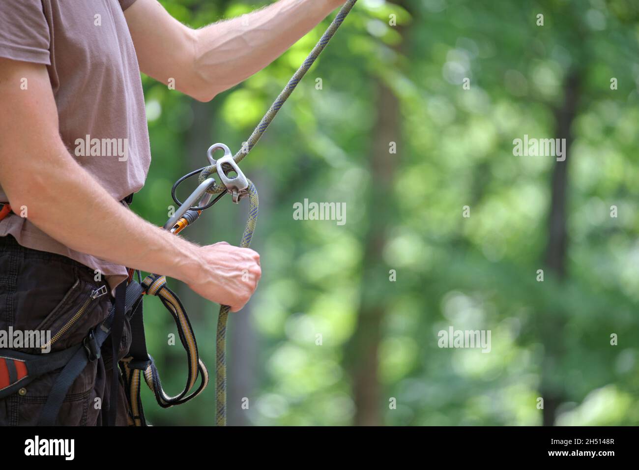 Man belays his partner climber with belaying device and rope. Climber's handsman holding