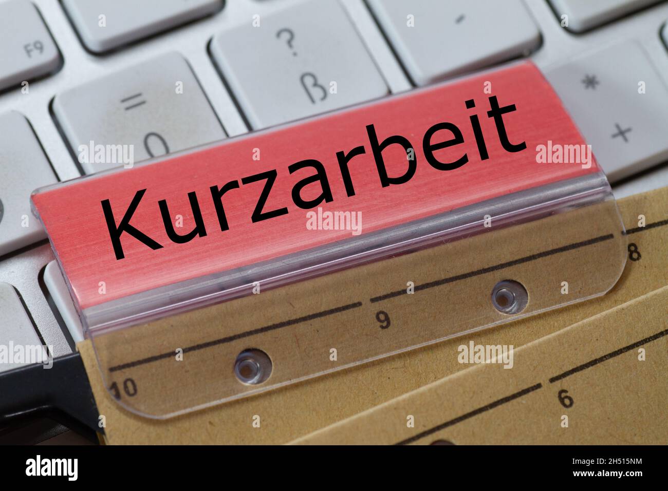 The German word for short-time work can be seen on the red label of a brown hanging folder. The hanging folder is on a computer keyboard. Stock Photo