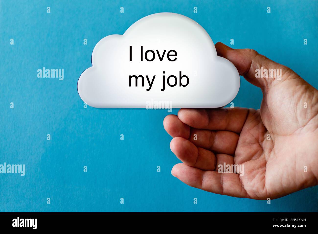 Hand holds a white cloud symbol against a blue background. The text is written on the cloud: I love my job Stock Photo