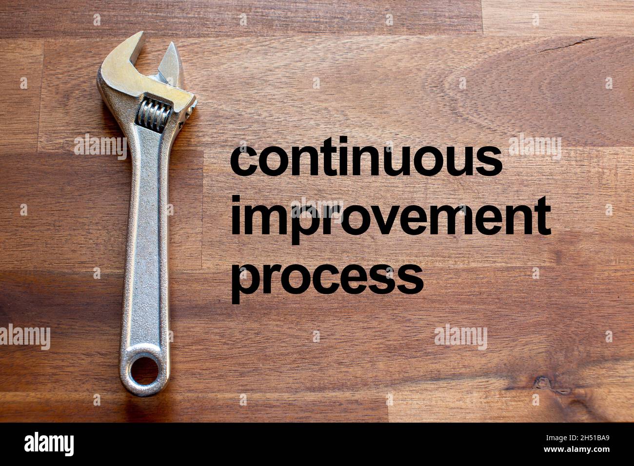 a flexible chromed adjustable wrench lies on a dark wooden table. The solgan continuous improvement process is written on the table in black letters Stock Photo