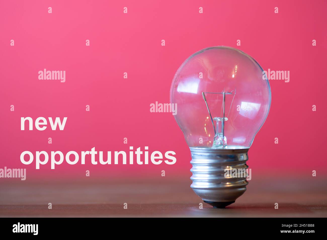 new opportunities are the words written in white on the red background  Next to the words, an ancient light bulb stands freely and upright on a dark w Stock Photo