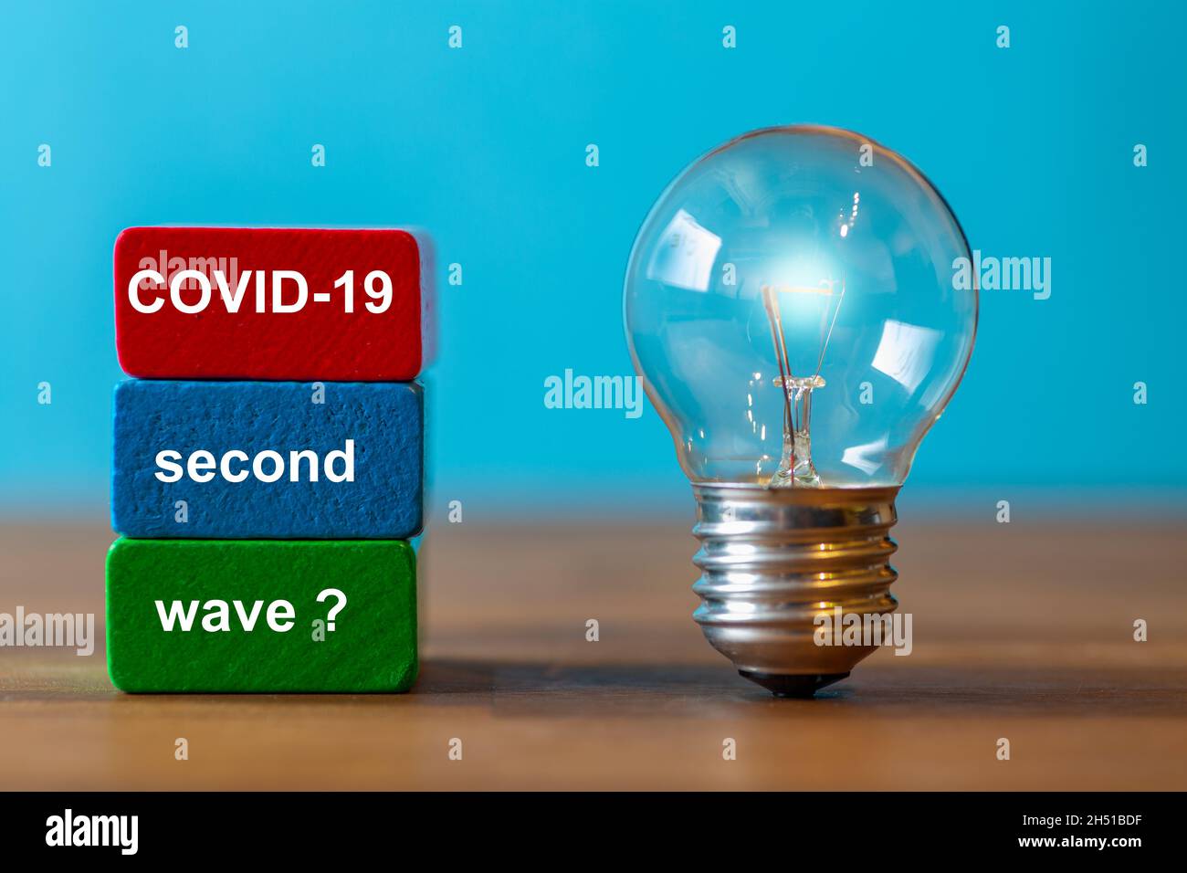 COVID-19 second wave? are the words written on a colored toy block. Next to the toy blocks, an ancient light bulb with glowing light stands freely and Stock Photo