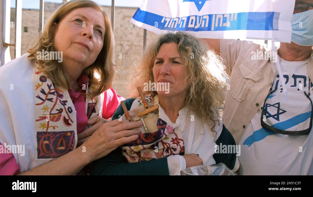 A member of the Women of the Wall holds a Torah scroll, as security forces hold back Ultra-Orthodox Jews protesting their prayer at the Western Wall on November 05, 2021 in Jerusalem, Israel. The Women of the Wall is a feminist prayer group that holds a monthly prayer session at the Western Wall and have consistently claimed that there is no single 'custom of the place' and that their right to pray is a religious freedom enshrined in Israeli law Stock Photo