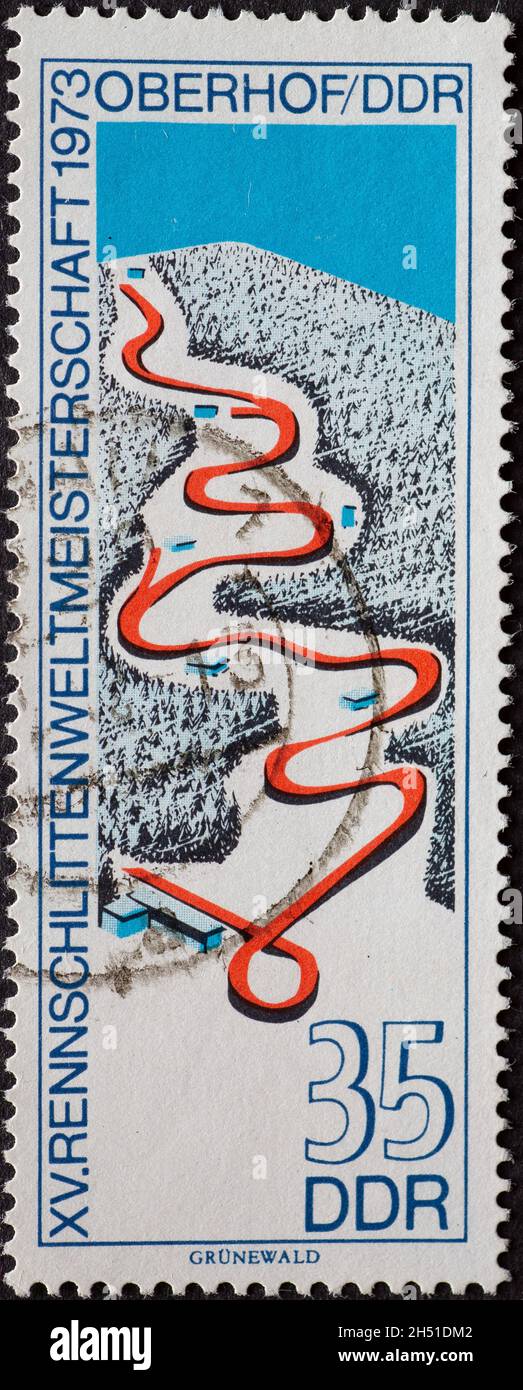 GERMANY, DDR - CIRCA 1973 : a postage stamp from Germany, GDR showing the racing sled racetrack on the mountain. Text: Racing sled world championship Stock Photo