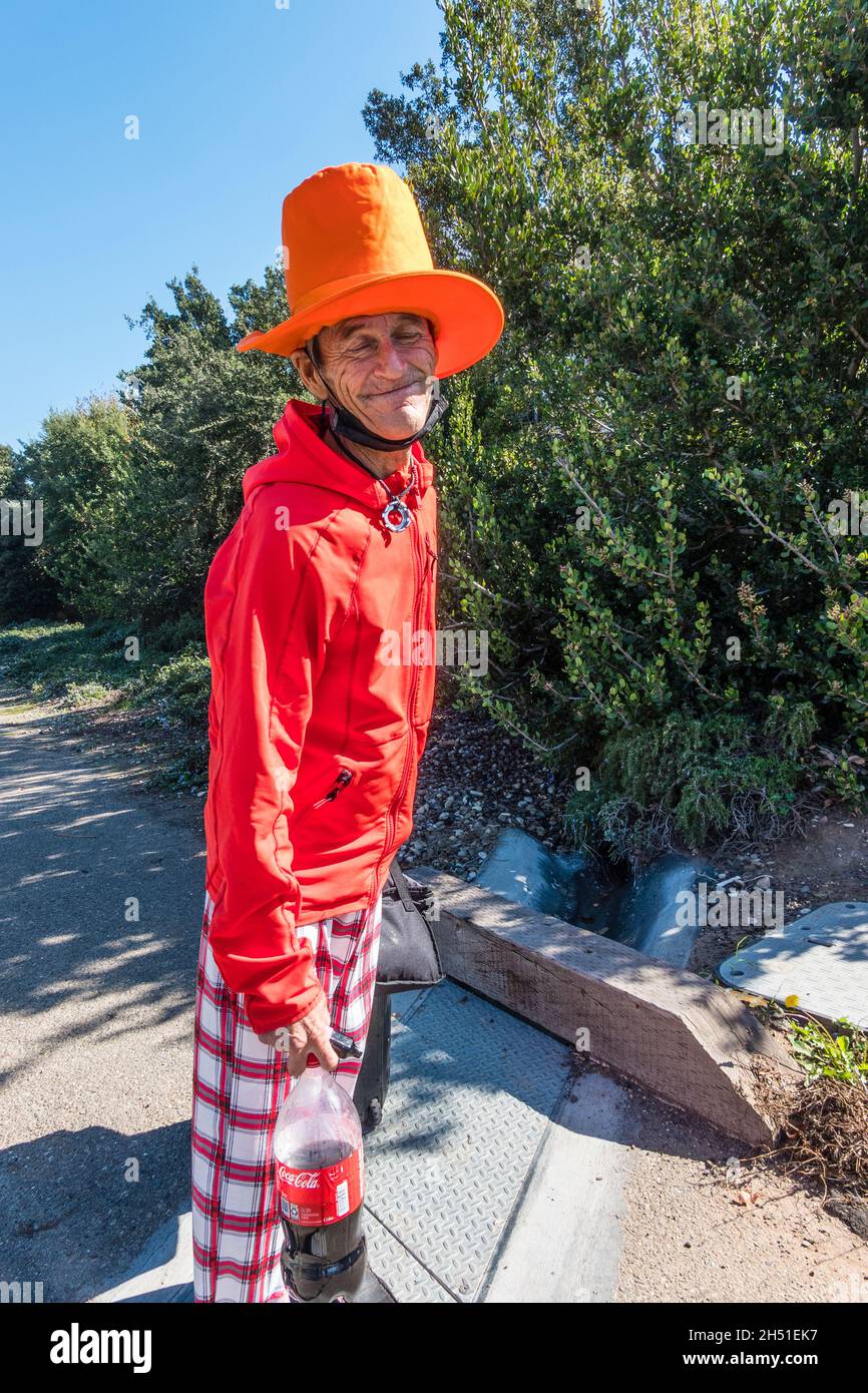 Rand, the street person, dressed in bright colors of red and orange, walks along State Street in Santa Barbara County with his very tall orange hat. Stock Photo