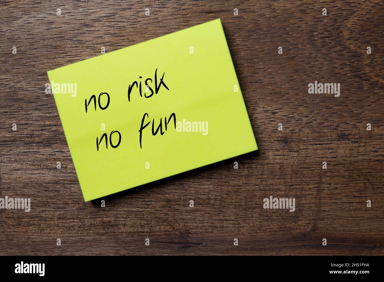 yellow self-adhesive note sticker diagonally on a dark wooden table top with stylized handwriting with the text: no risk no fun Stock Photo