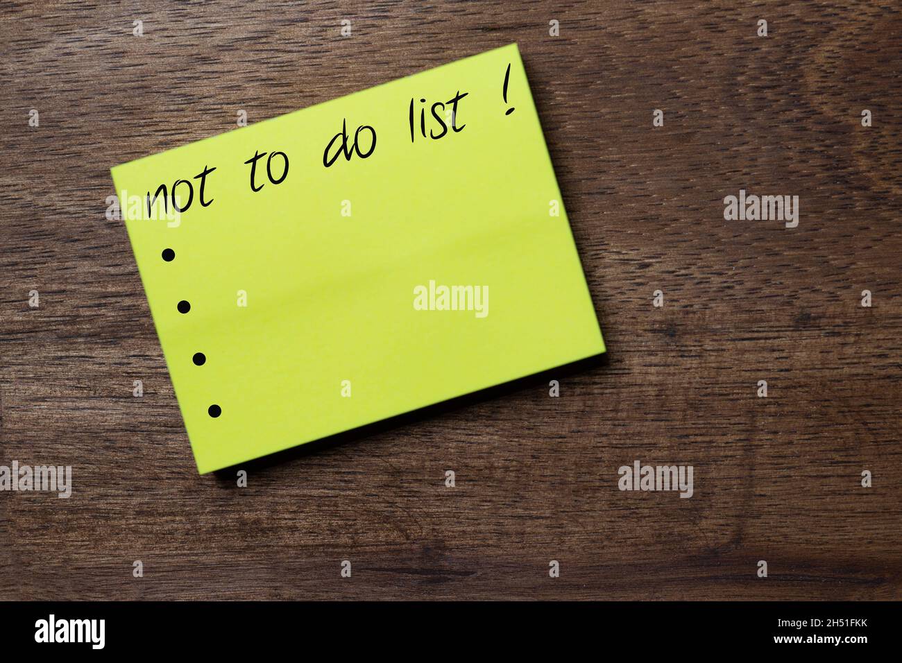 yellow self-adhesive note sticker diagonally on a dark wooden table top with stylized handwriting with the text: not to do list ! Stock Photo