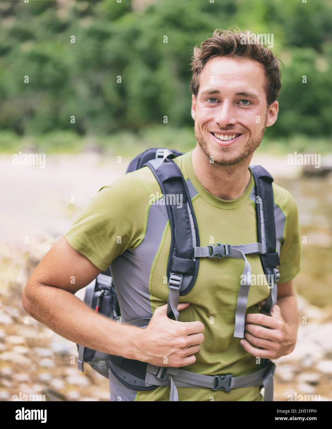 Active young man portrait hiking outdoors. Young male hiker smiling happy wearing backpack for backpacking camping travel trip outdoors during hike in Stock Photo