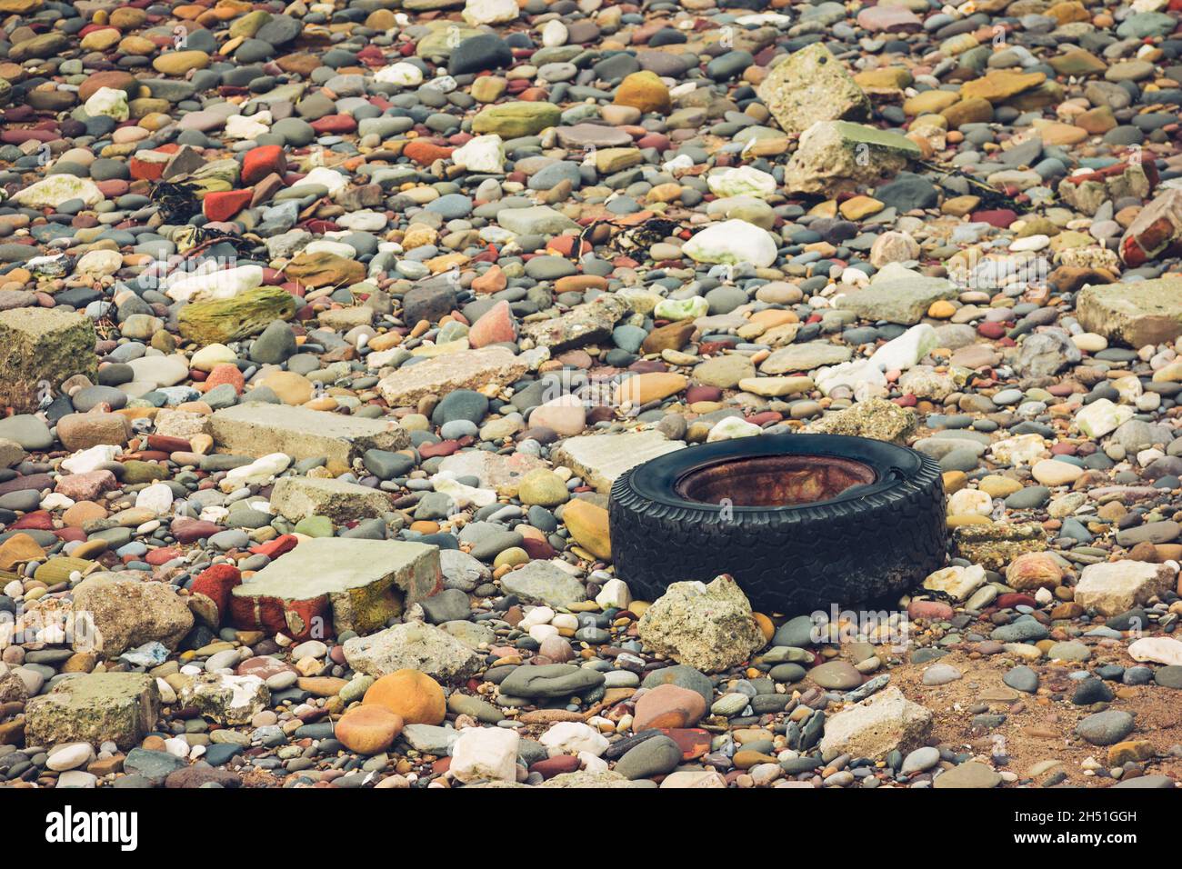 A black car tyre washed onto a colourful shingle beach as marine debris Stock Photo