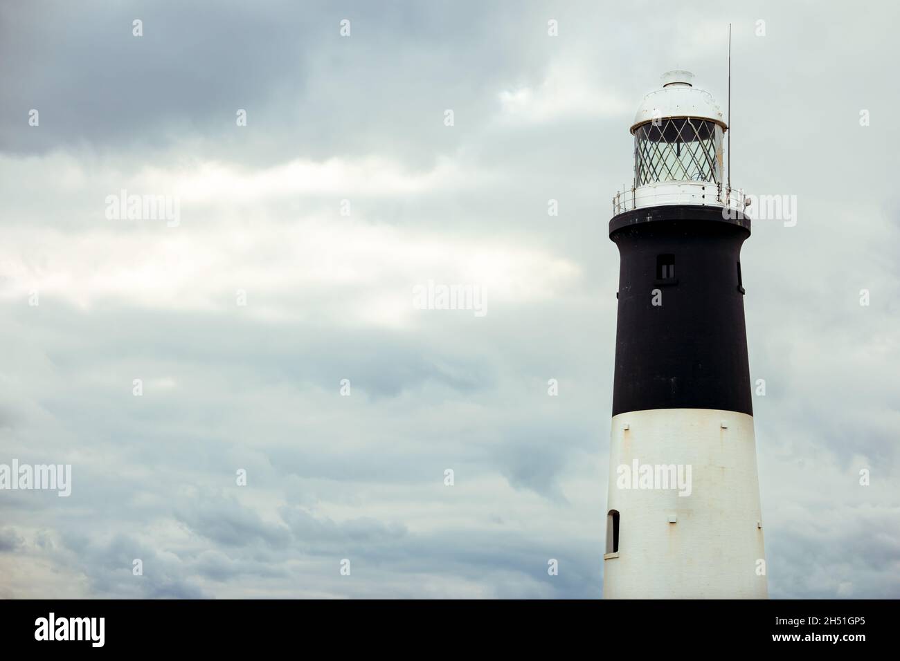 Close up of a cylindrical brick tower lighthouse with black and white bands with white space Stock Photo