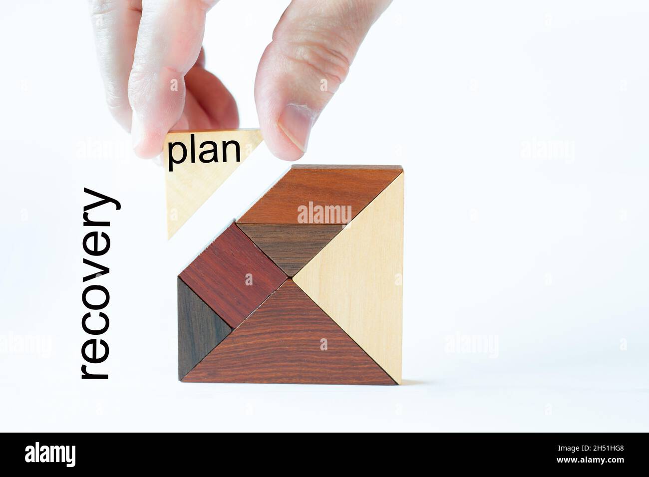 A missing stone is inserted into a noble wooden tagram by one hand. The text plan is written o a block and on the background and the text recovery is Stock Photo