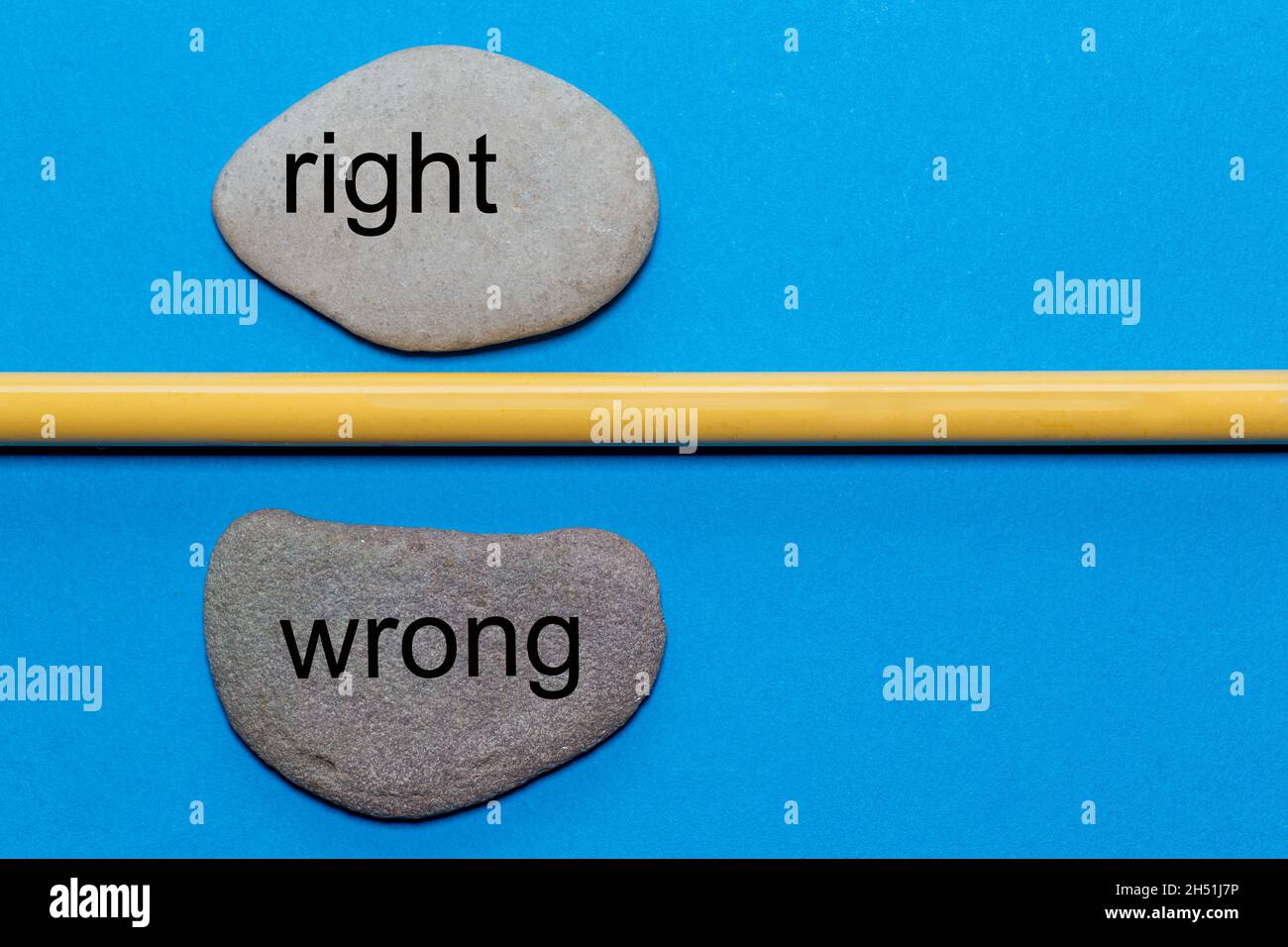 The words right and wrong are written on natural smooth stones separated by a yellow pencil. The background is isolated in blue and has a lot of space Stock Photo