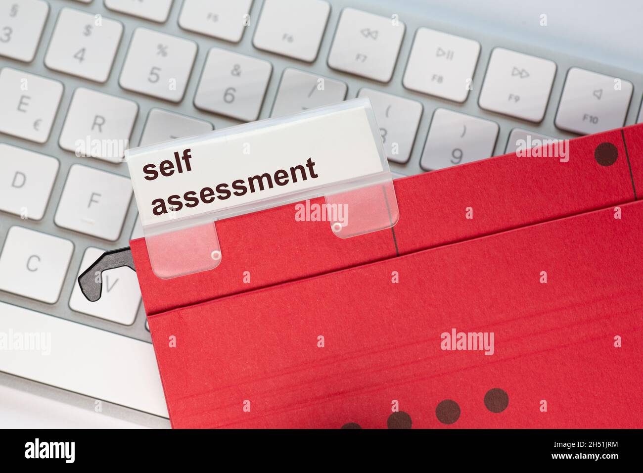 red hanging folder on a keyboard has a tab with the words: self assessment on it Stock Photo