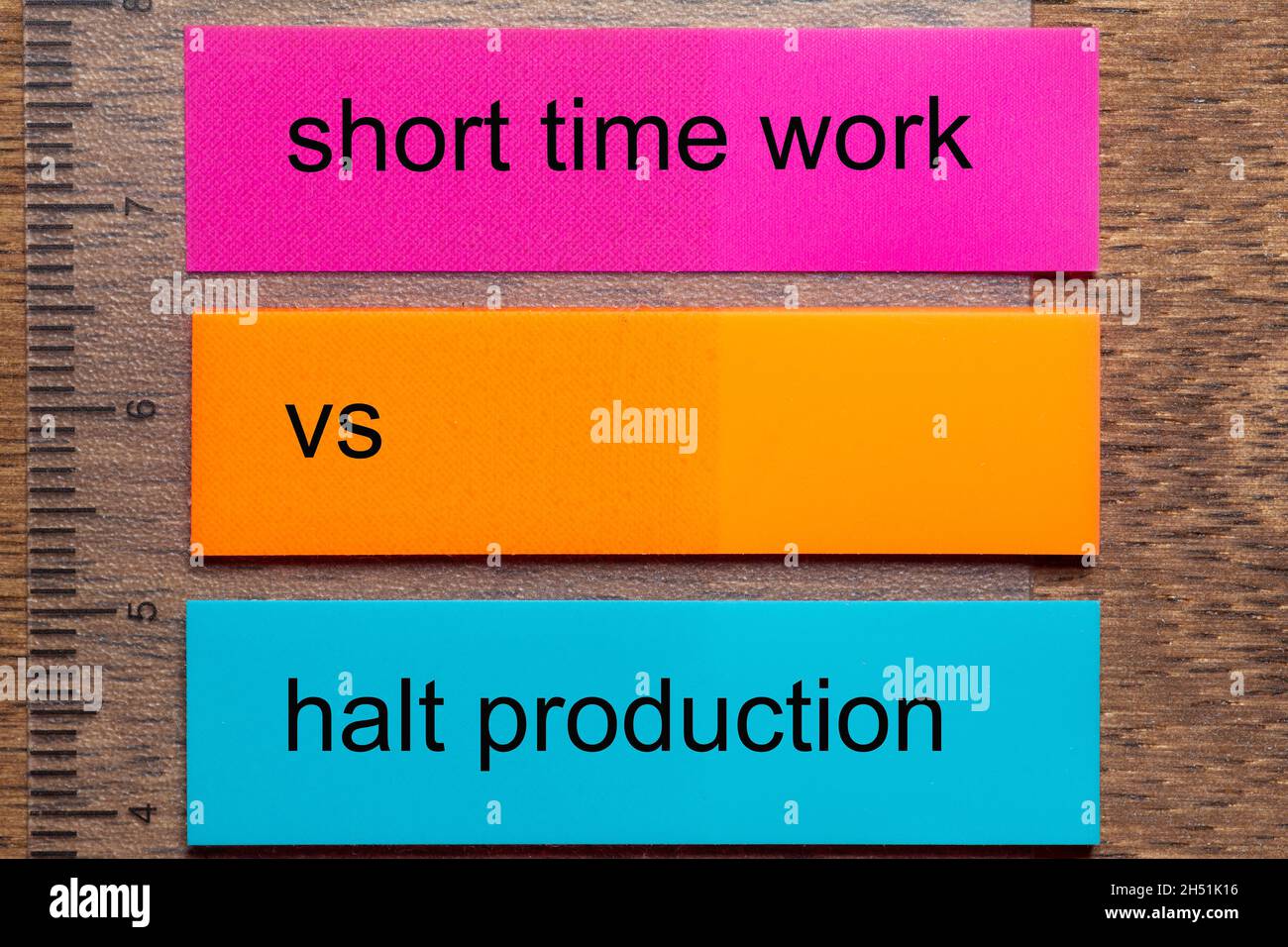 Three bookmark stickers with the words short time work vs halt production, on a dark natural wooden table Stock Photo