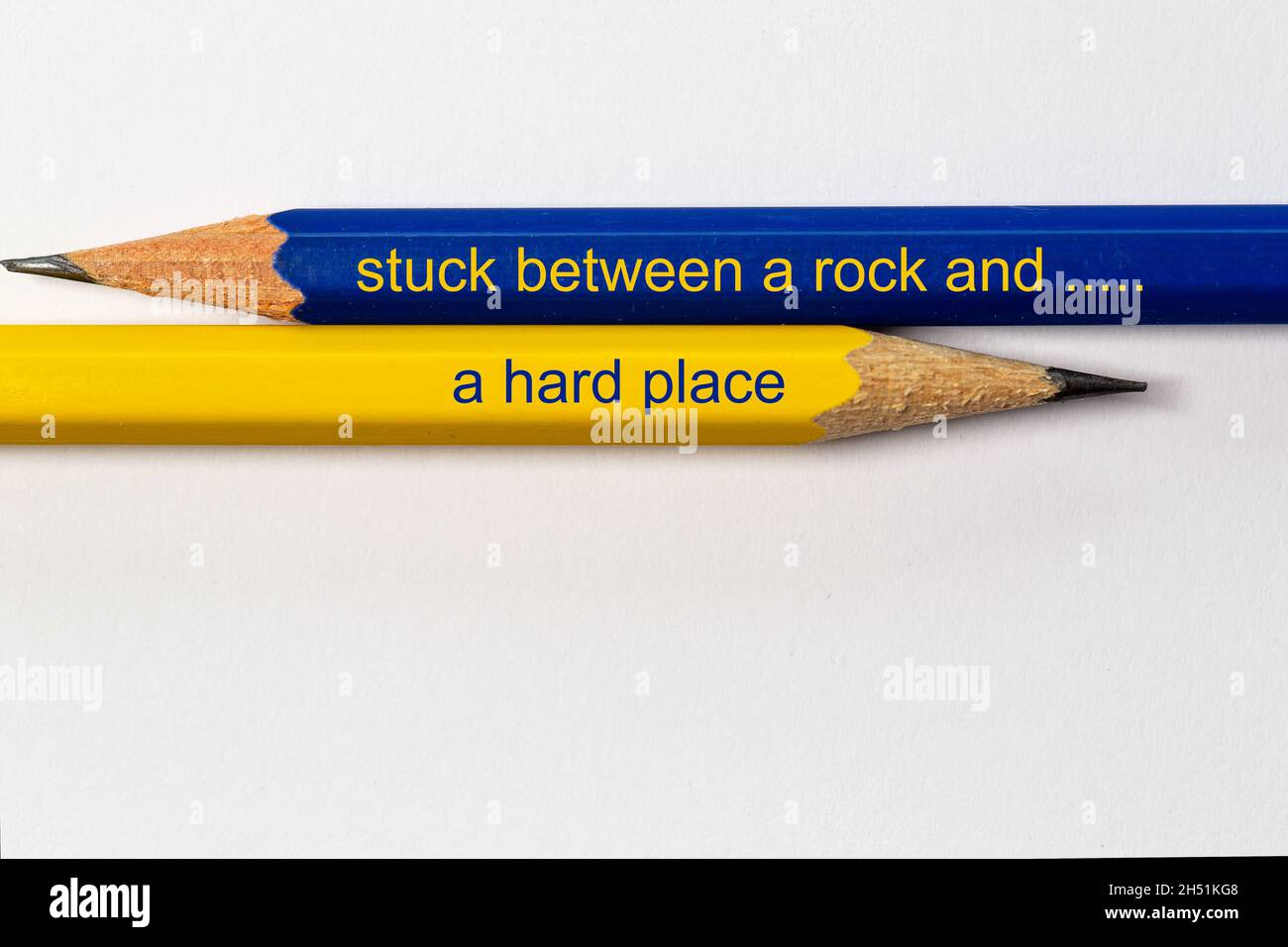 two sharpened pencils in blue and yellow point in different directions isolated against a white background with the conflicting wisdom: stuck between Stock Photo