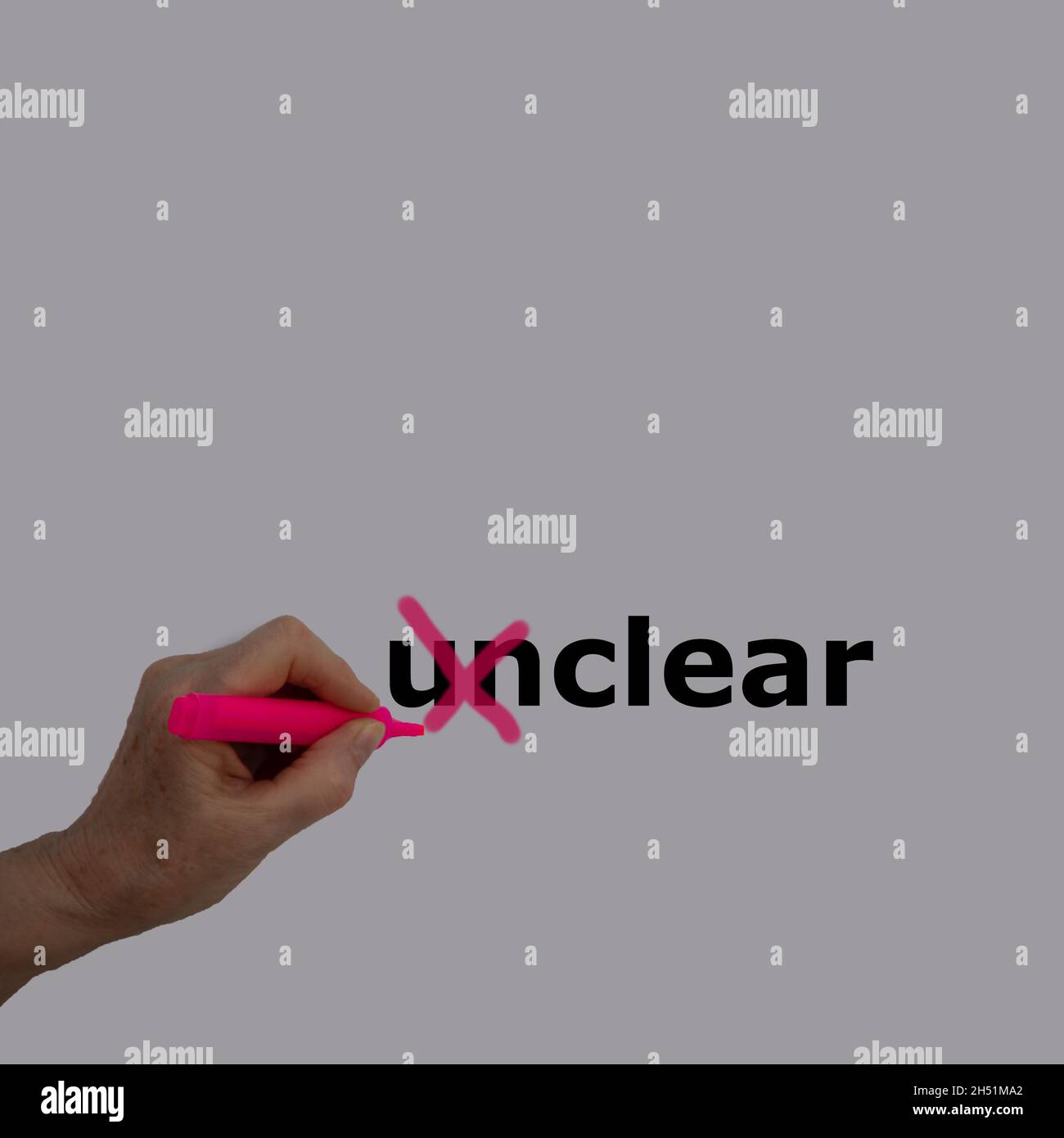 The prefix 'un' of the word unclear is crossed out with a pink pencil by a female hand Stock Photo