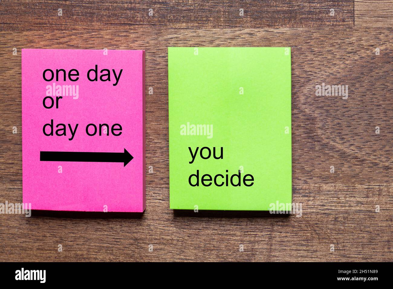 pink and yellow note stickers with the phrase: one day or day one you decide. The Background is a dark wooden table Stock Photo