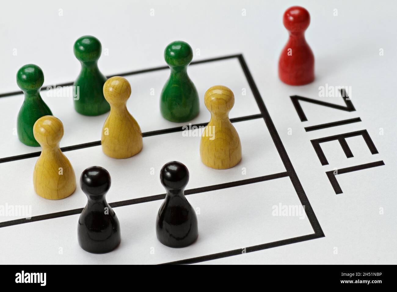Game pieces in red, green, yellow and black. Are competing to achieve a goal. The German word for target 'Ziel'  is written on the pad Stock Photo