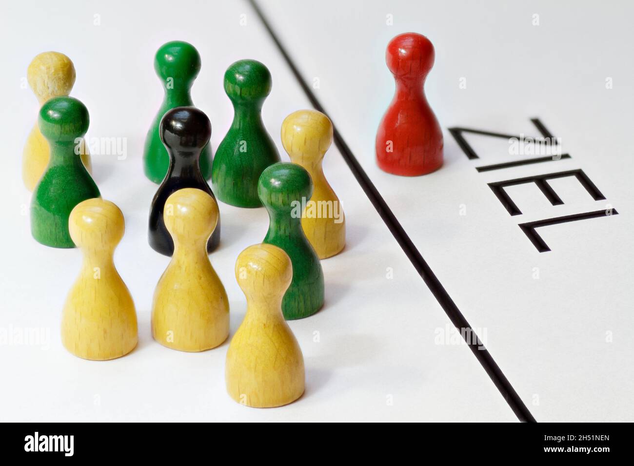 Game pieces in red, green, yellow and black. Are competing to achieve a goal. The German word for target 'Ziel' is written on the pad Stock Photo