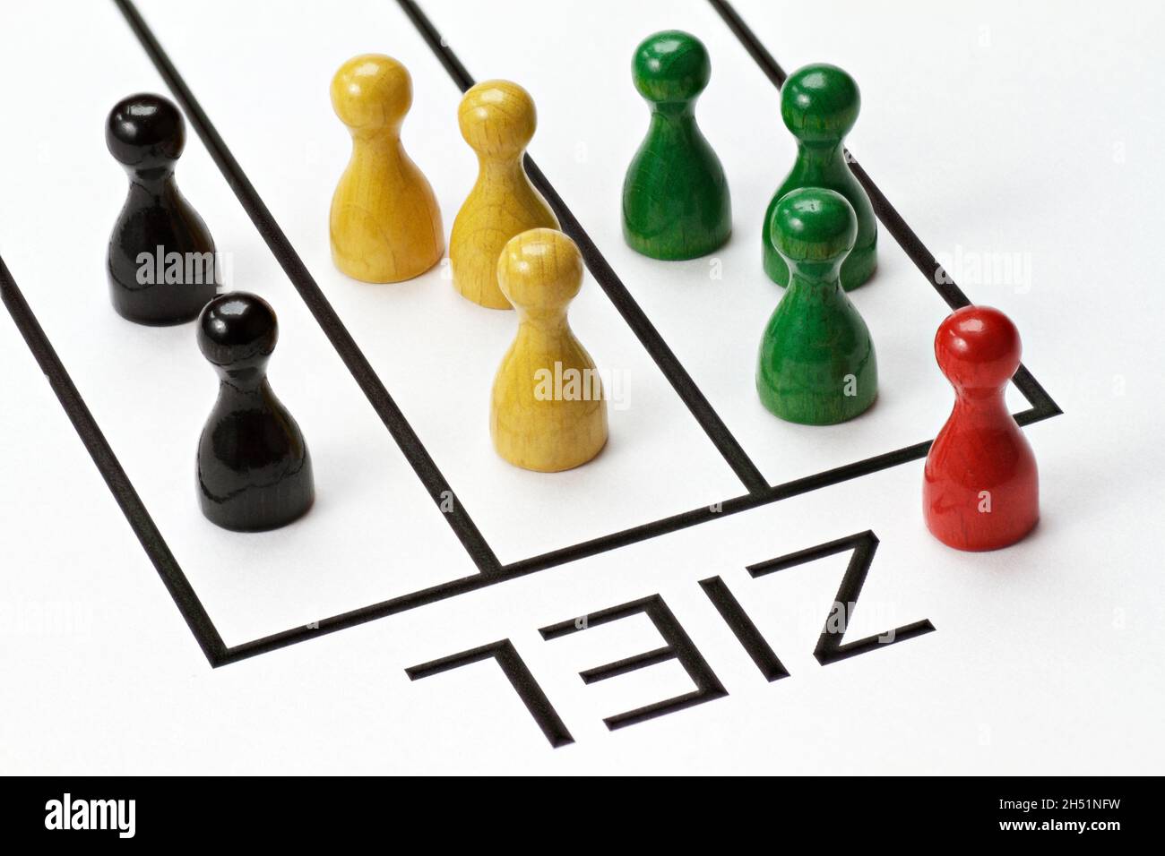 Game pieces in red, green, yellow and black. Are competing to achieve a goal. The German word for target 'Ziel'  is written on the pad Stock Photo