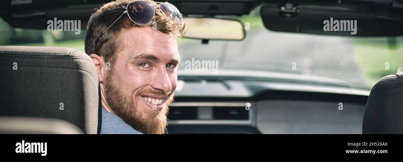 Car driving man driver smiling portrait. Young adult sitting in front seat of new convertible sports car. Panoramic header crop banner. Stock Photo