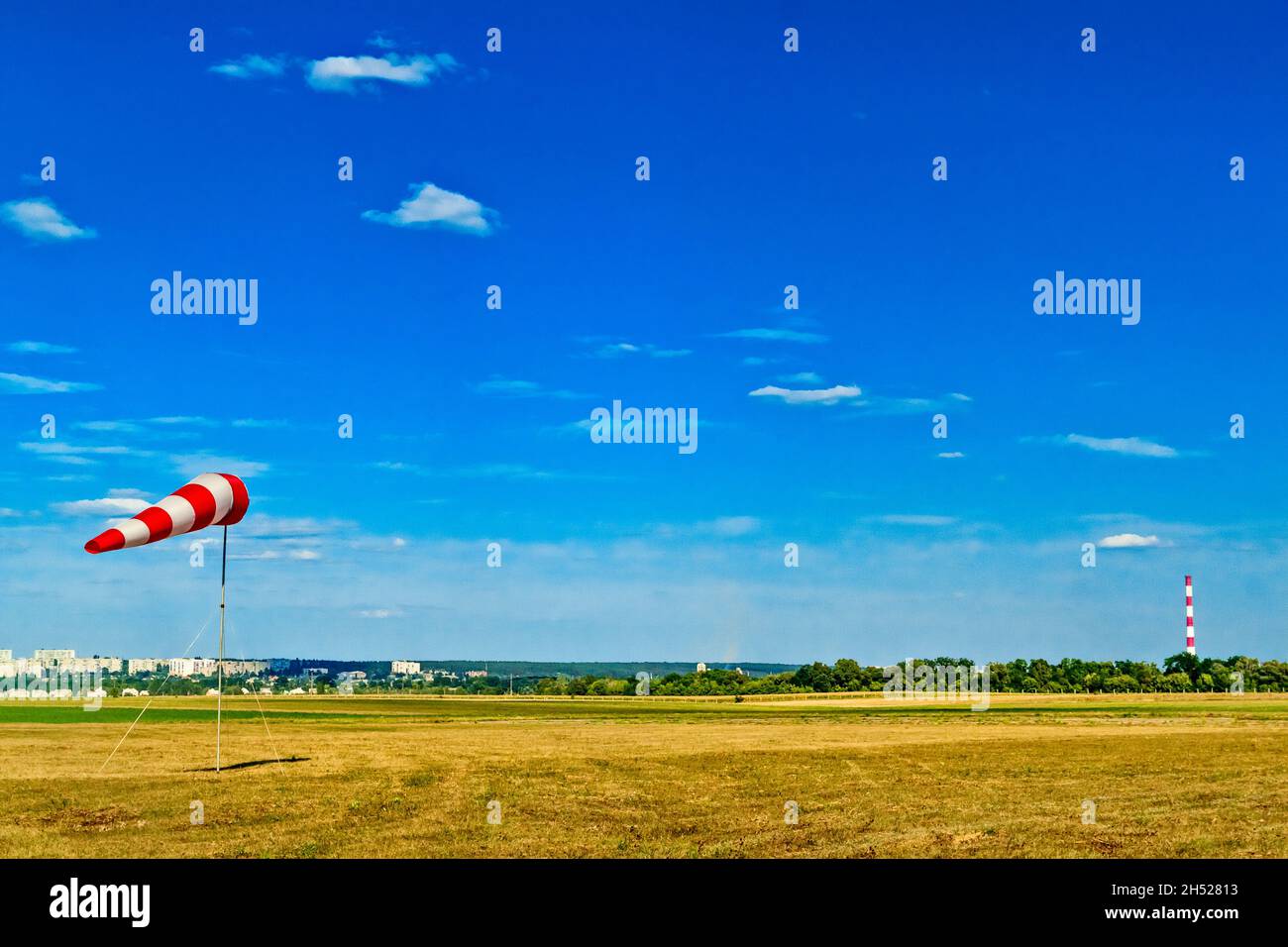 Red and white windsock wind sock on blue sky, green field and clouds background on aerodrome or airdrome. Shows wind speed and direction. Stock Photo