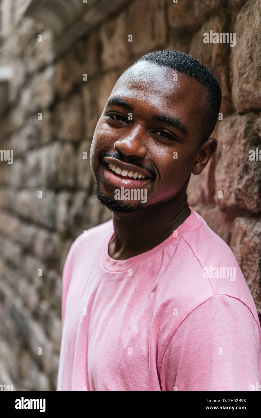 vertical portrait of an afro american young man. He is looking at camera with a stone wall on the background Stock Photo
