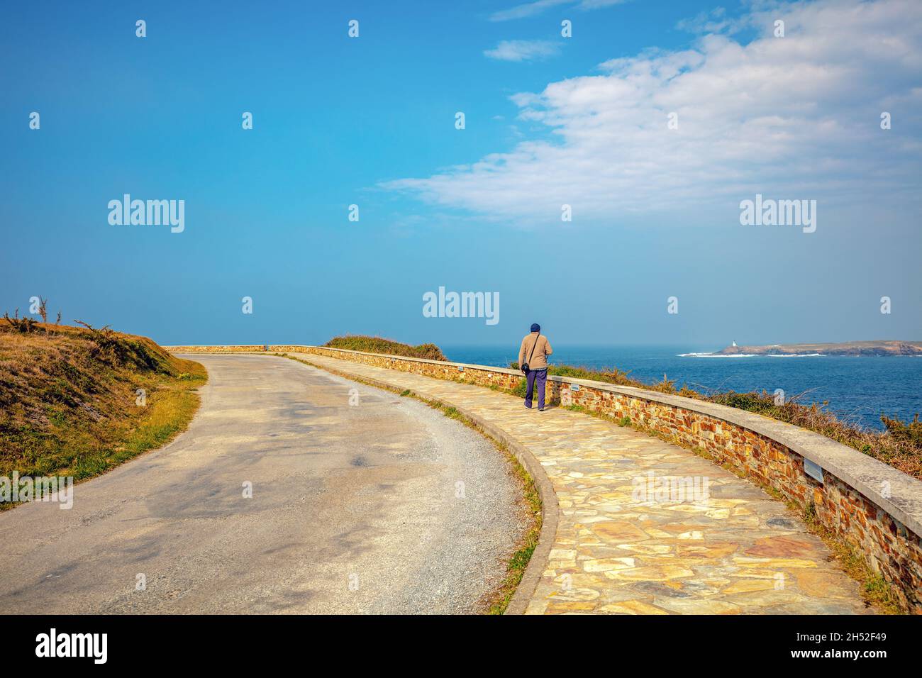 A man walks along the promenade Lighthouse road (Estrada do faro) along the sea on a sunny day Stock Photo