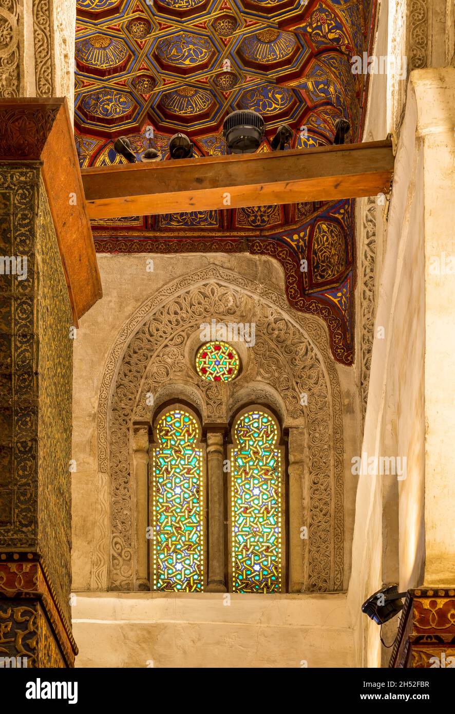 Two adjacent perforated stucco arched windows decorated with colorful stain glass with geometrical and floral patterns, at Mamluk era public historical Qalawun complex, Moez Street, Cairo, Egypt Stock Photo